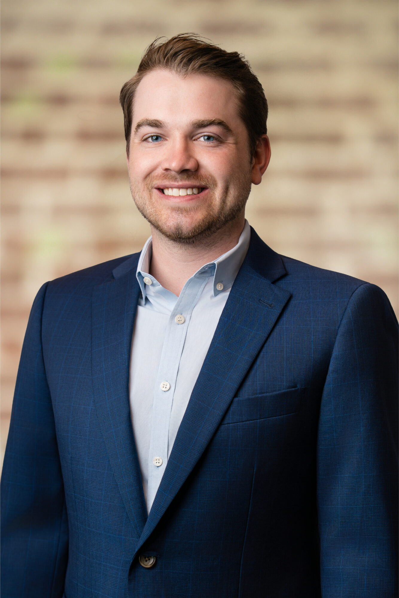 Grady Cotham, Senior Retail Associate at Jones Aur Commercial Real Estate, smiling in a blue suit against a blurred brick background, representing expertise in Memphis commercial real estate and client representation.