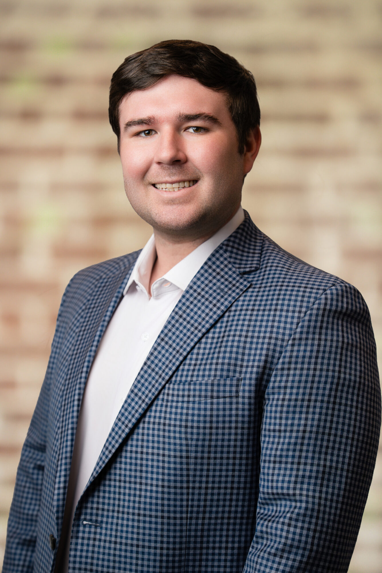 Hudson Cunningham, Operations Coordinator at Jones Aur Commercial Real Estate, smiling in a professional setting with a brick background, representing Memphis commercial real estate expertise.